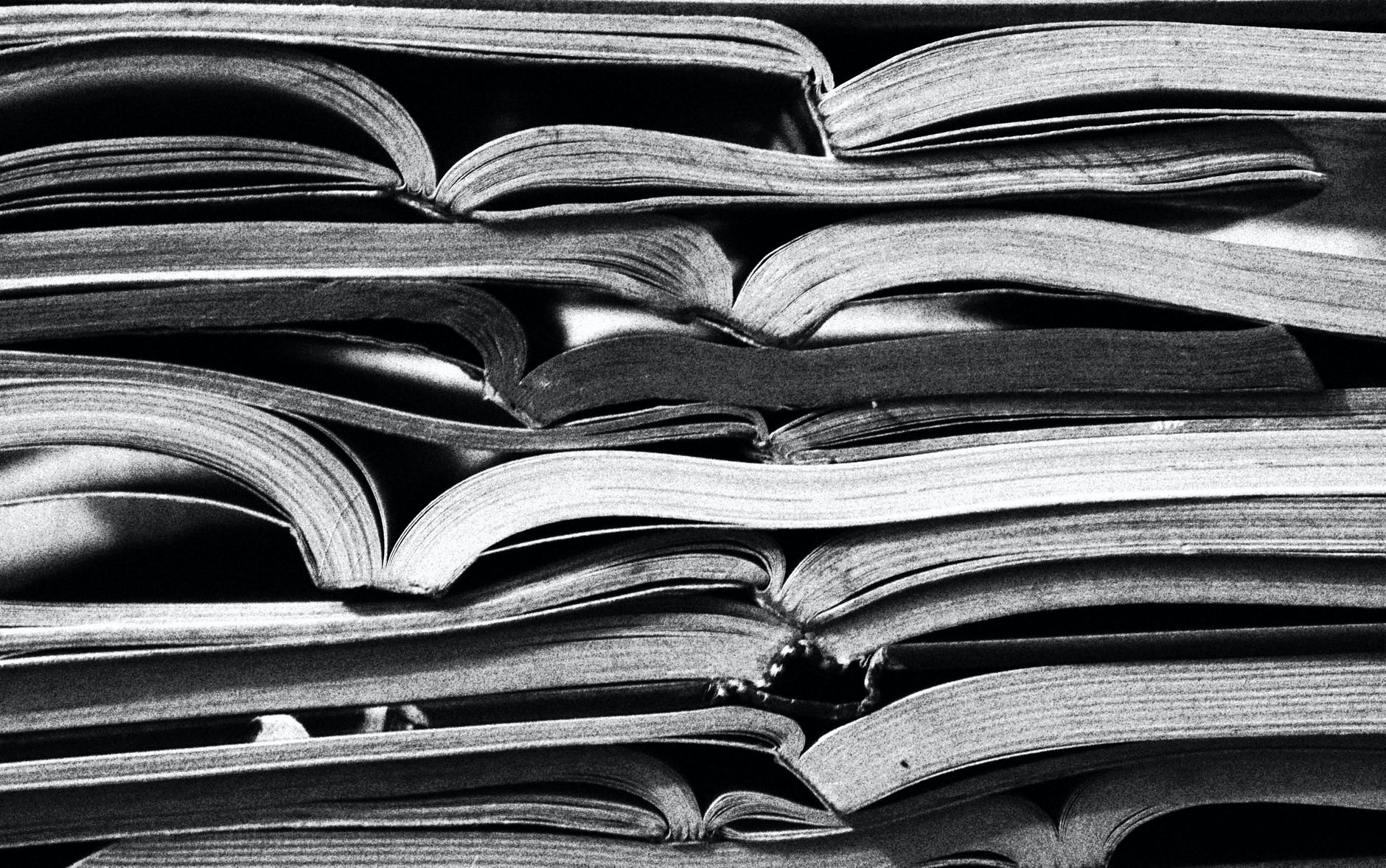 Black and white picture of opened books piled on top of one another. Photo by Ferbugs on Pexels.com.